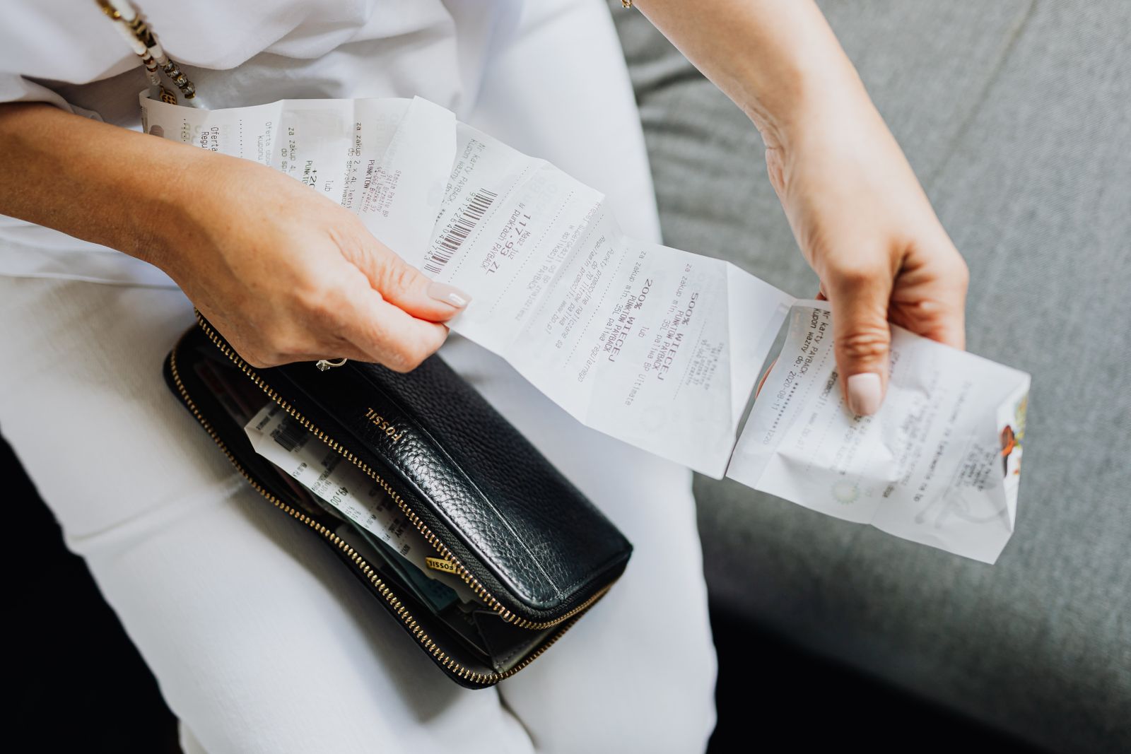 A handful of paper receipts being sorted over an open purse